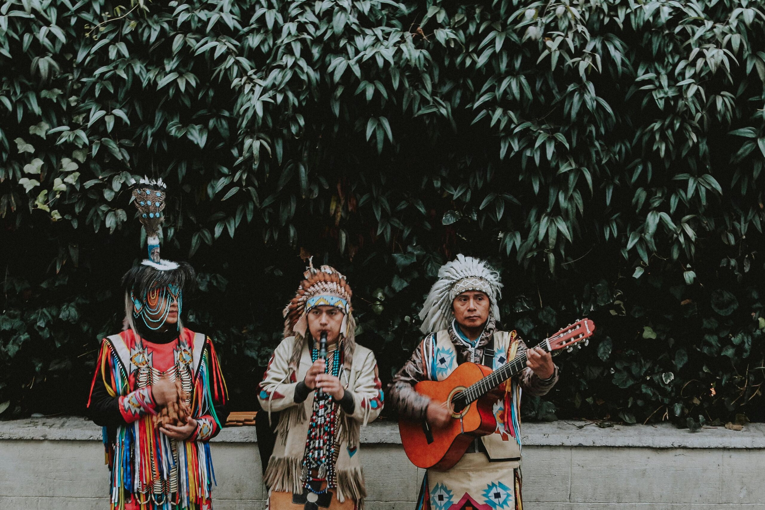 Three Men in Traditional Native American Clothes Playing Guitar on Side of Road