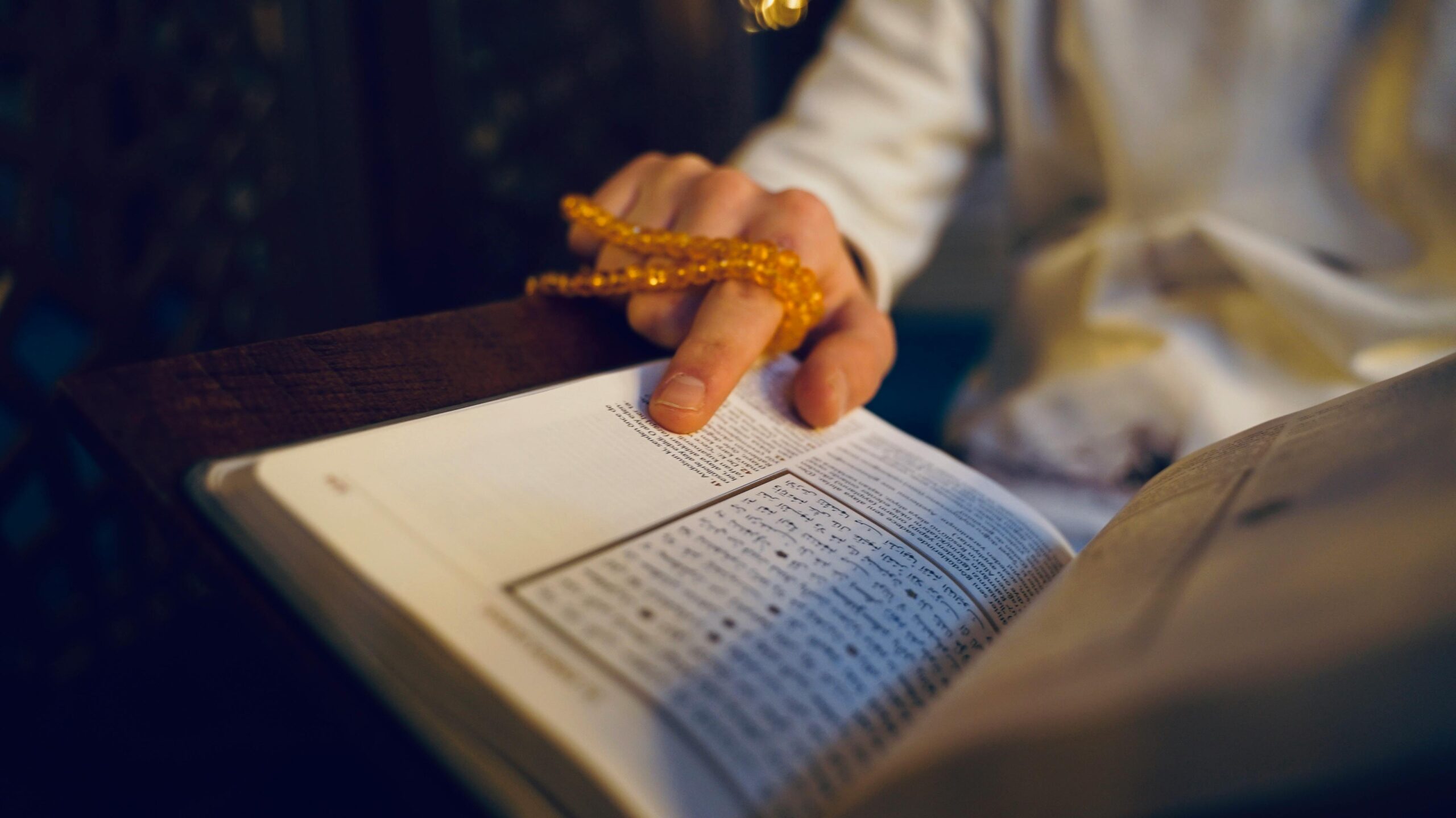 Close-up of a person reading religious text with prayer beads in hand, symbolizing faith and spirituality.