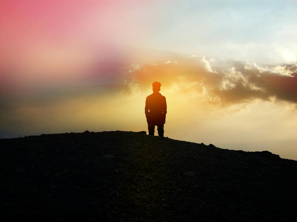 A silhouette of a person standing on a hill with a colorful sunset background, evoking calm and reflection.