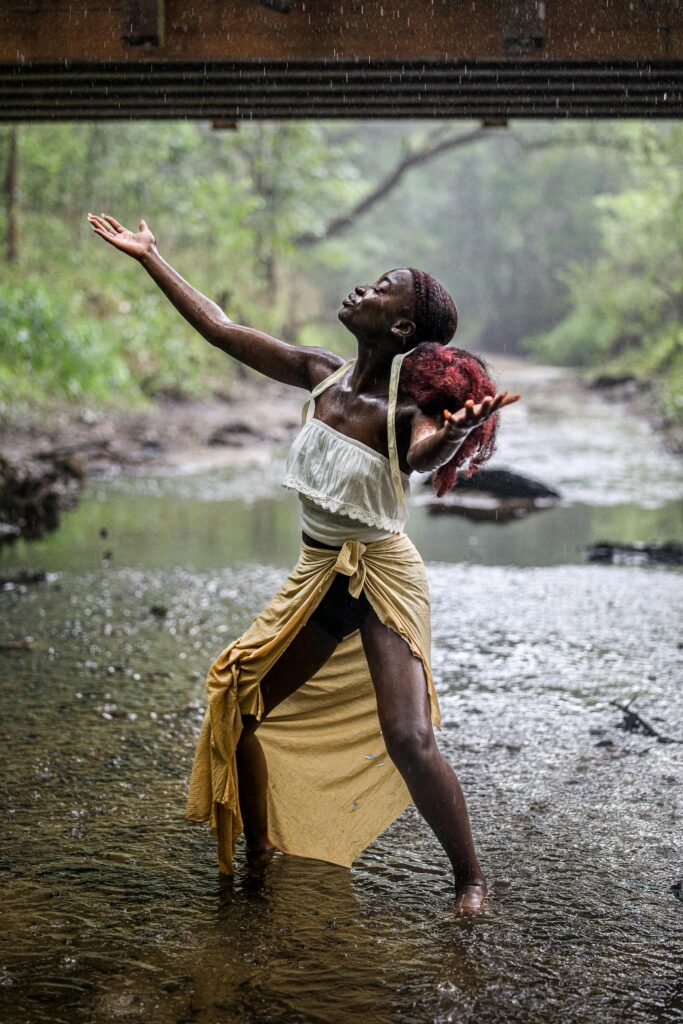 An expressive African woman enjoying the rain in a natural setting, symbolizing freedom and happiness.