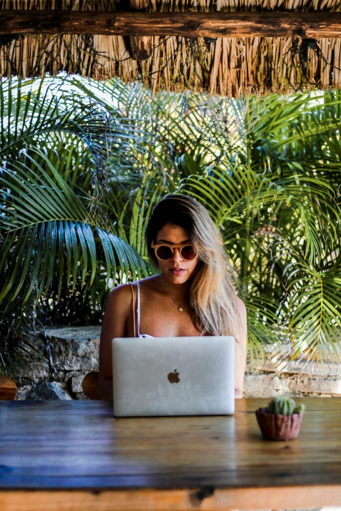 A woman using a laptop outdoors surrounded by lush greenery.