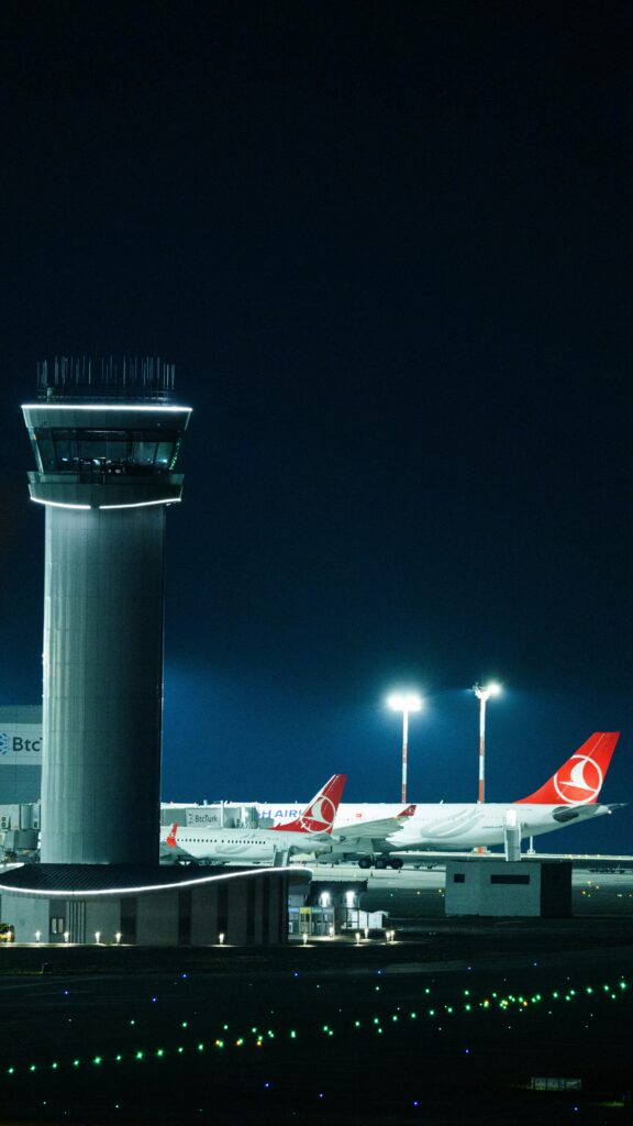 Illuminated control tower and Turkish Airlines planes at Istanbul Airport during nighttime.