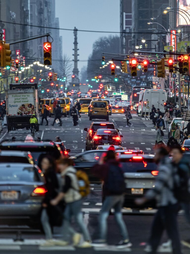 A vibrant city street in New York with traffic and pedestrians during evening rush hour.