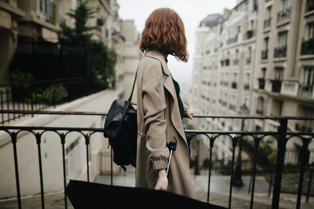 Woman in trench coat walking through a Parisian street with an umbrella, showcasing city life and travel.