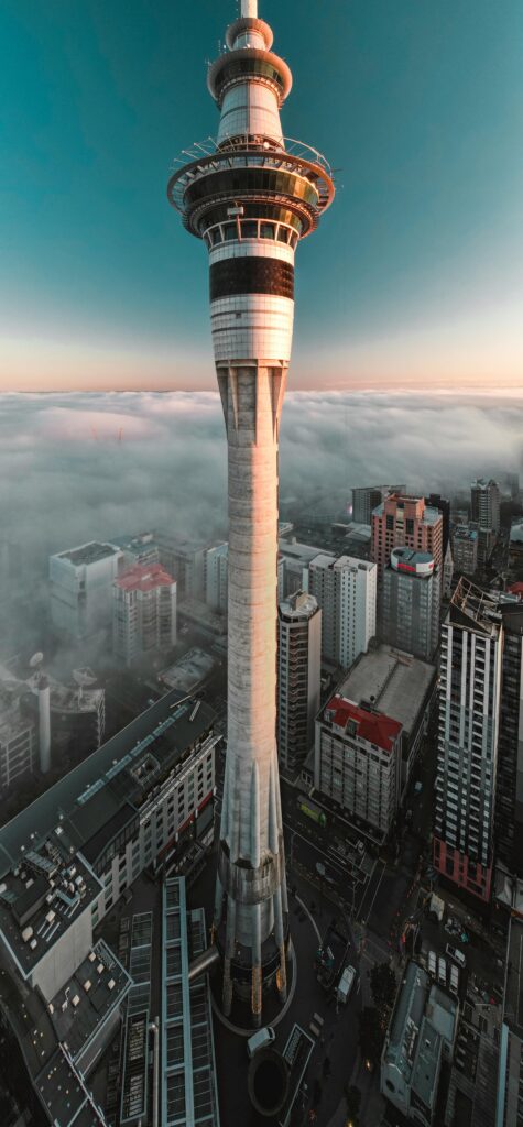 Captivating aerial view of Auckland's iconic Sky Tower surrounded by fog at sunrise.