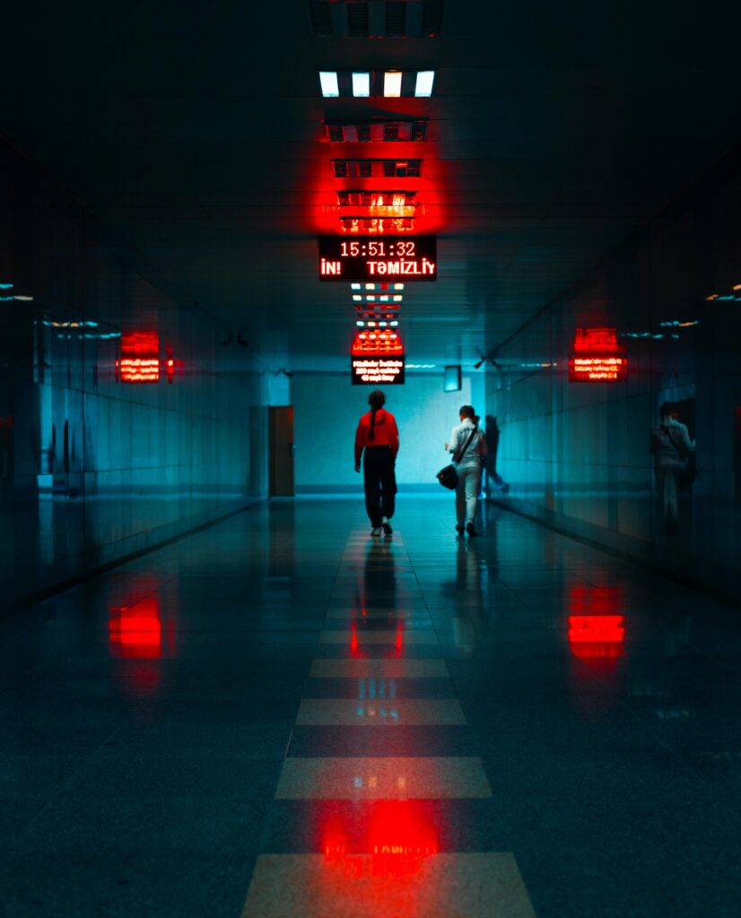 Travelers walking through a futuristic terminal hallway in Baku, reflecting vibrant red and blue lights.