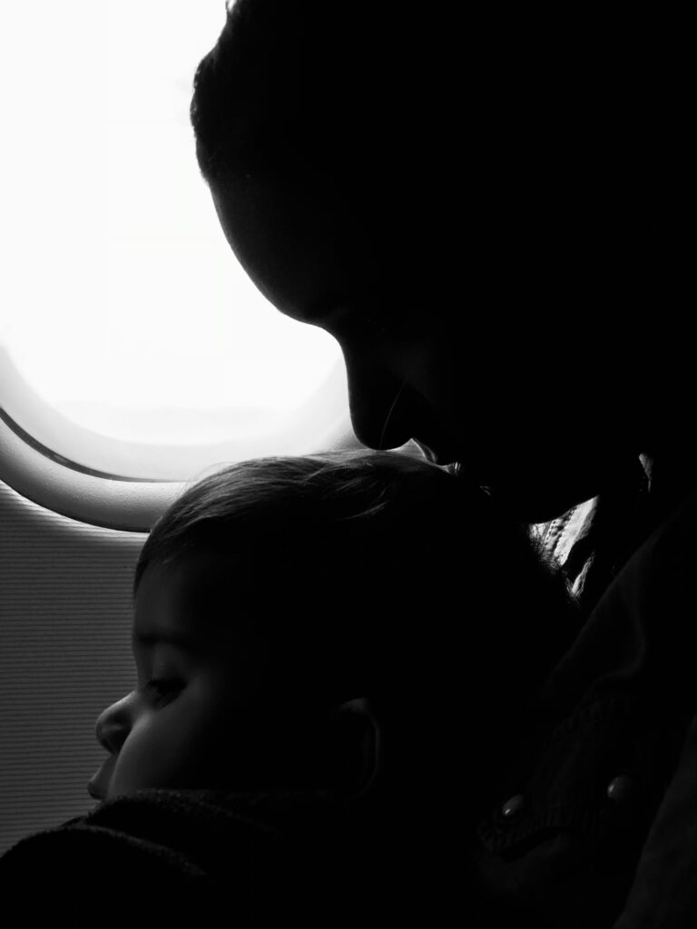 Silhouette of a mother and child gazing out an airplane window during flight.