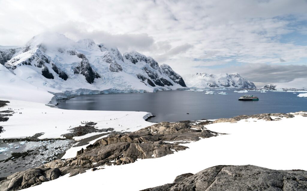 Scenic Antarctic view with icy mountains, calm waters, and a solitary boat.