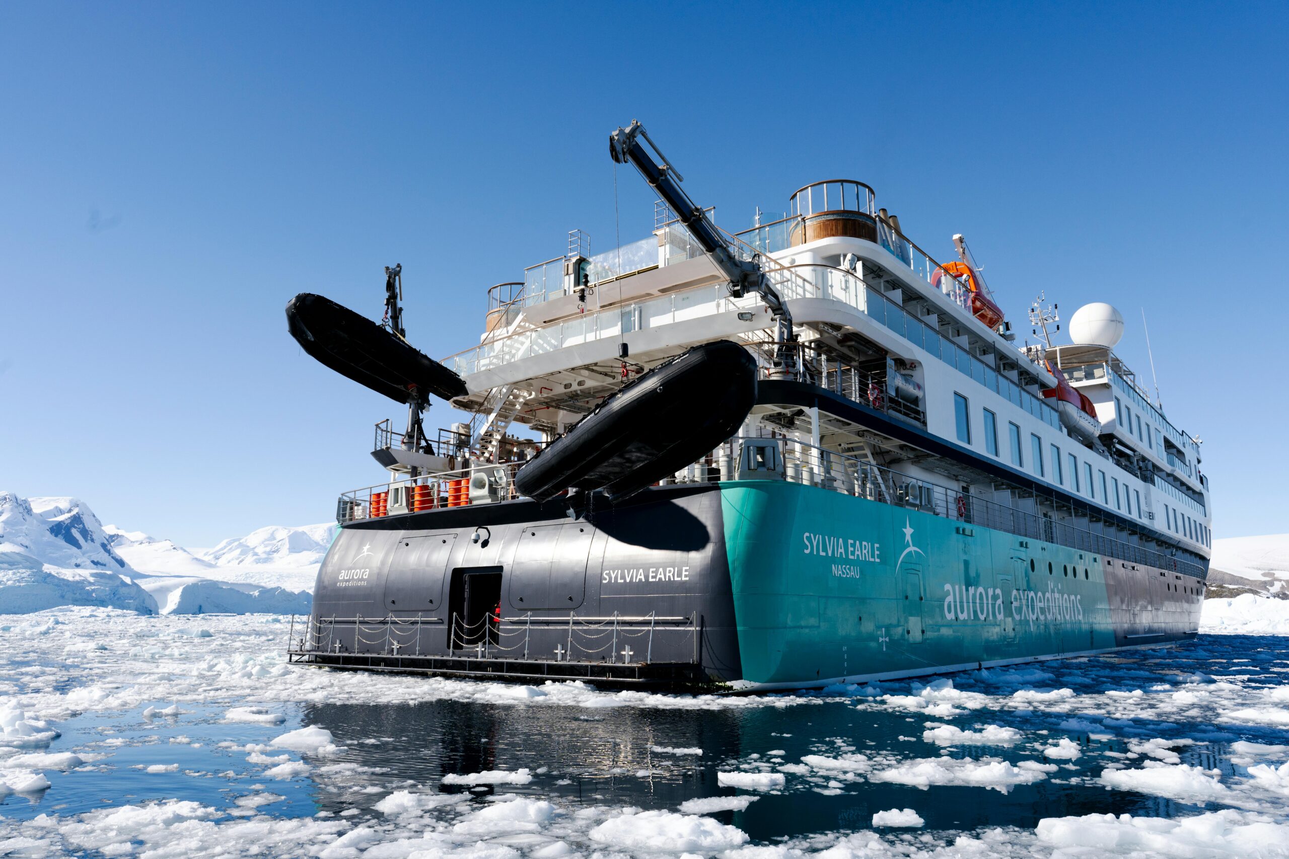 The expedition ship Sylvia Earle navigating icy waters in the Arctic, surrounded by stunning icebergs and clear skies.