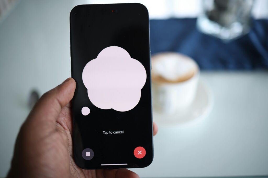 Close-up of a smartphone in hand with AI voice chat bubble and coffee in background.