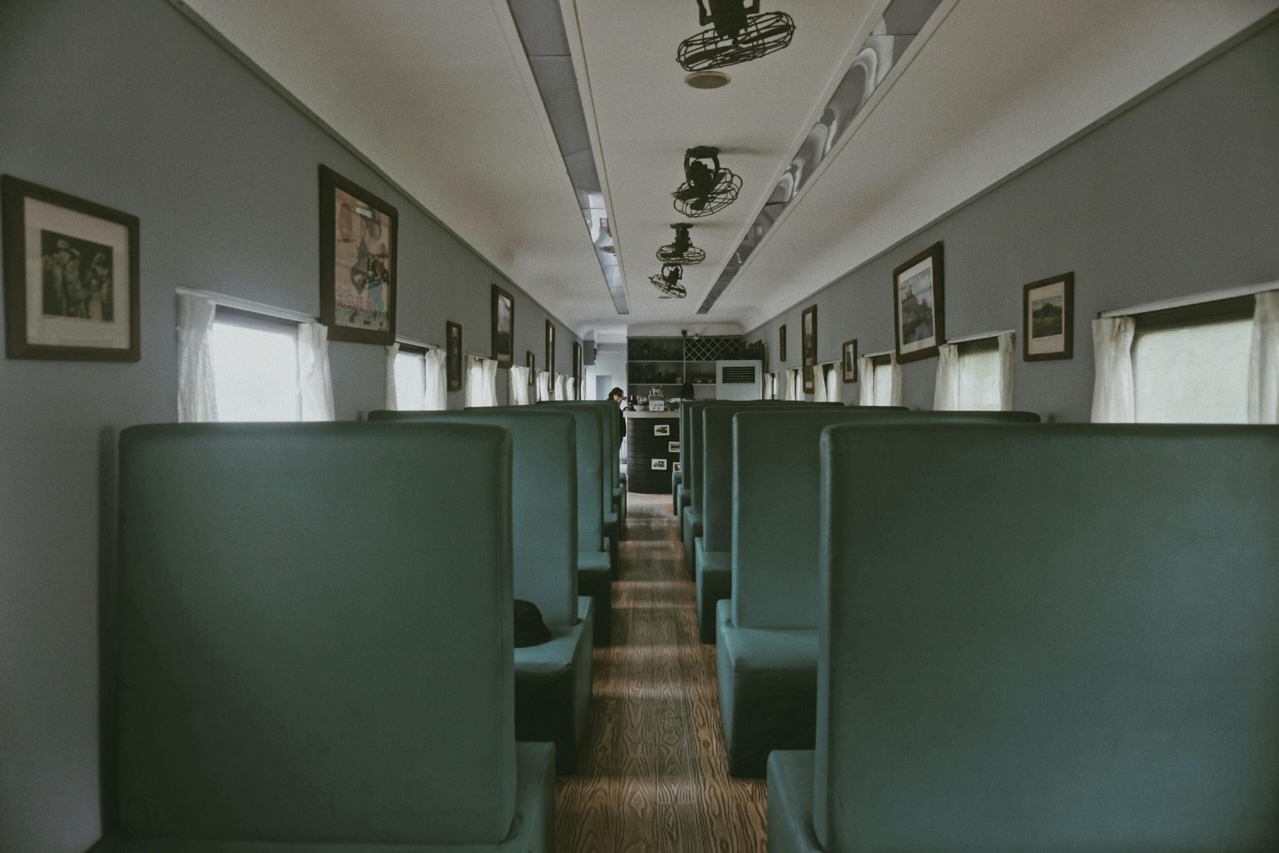 A sleek and modern interior of a contemporary train dining car, featuring green seats and framed artwork.