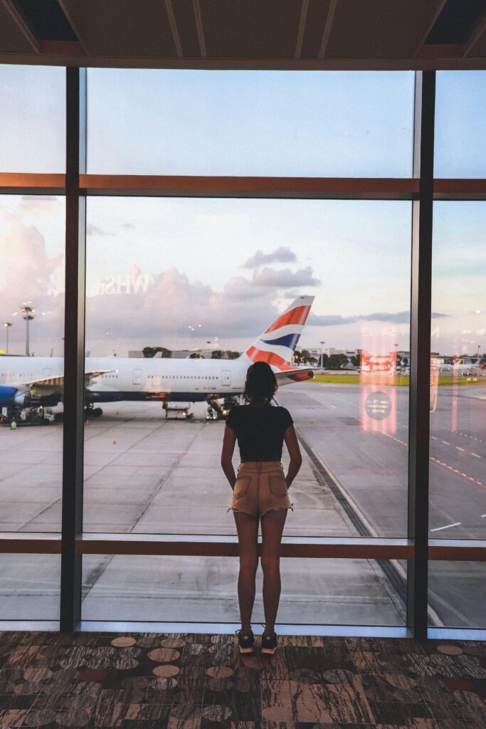 A woman stands at a glass window viewing airplanes at Singapore Airport, capturing the essence of travel and anticipation.