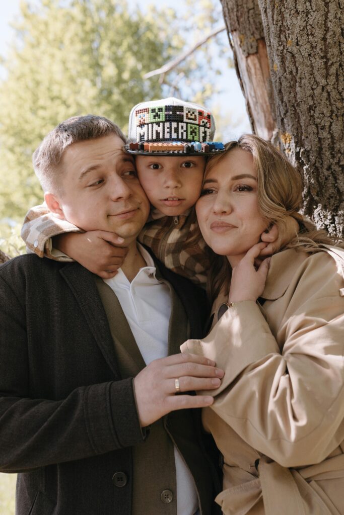 A joyful family of three sharing a warm embrace in a sunny park setting.