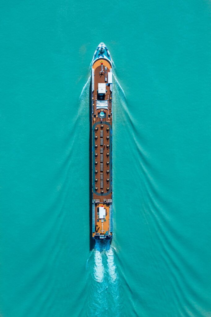 Drone shot of a cruise ship navigating turquoise waters, creating ripples and waves.