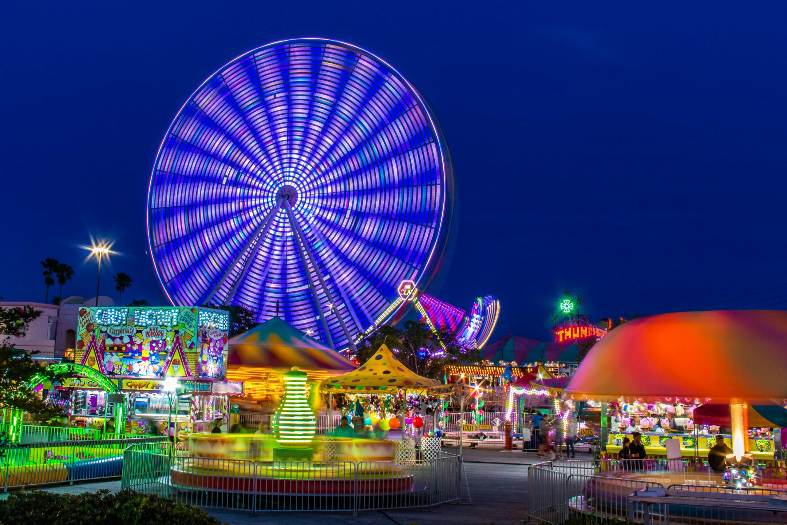 Brightly lit amusement park with a spinning Ferris wheel at night.