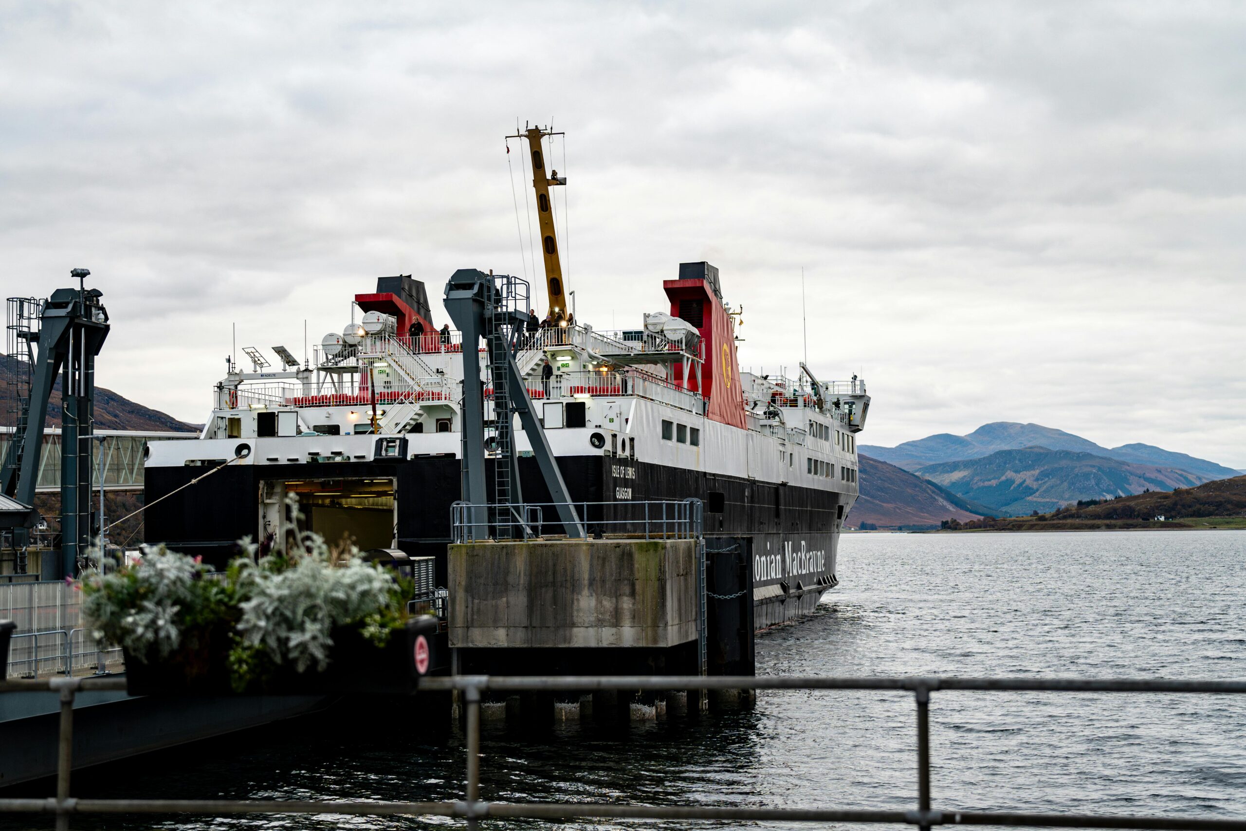 A large ferry ship docked at a pier amidst scenic mountains and water.