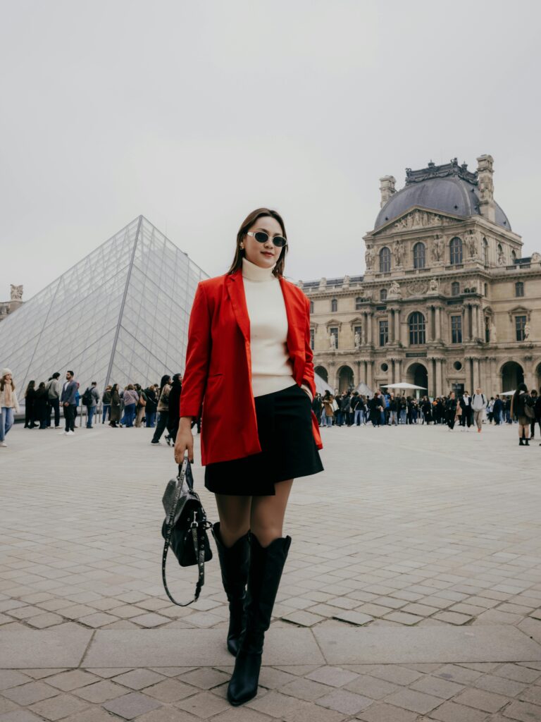 Stylish woman in red outfit posing at Louvre Pyramid, Paris.