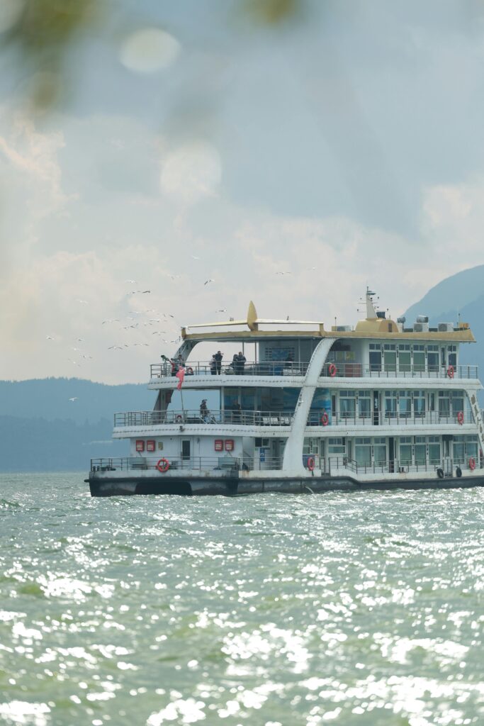 Passenger ferry cruising on a calm lake with a scenic mountain backdrop under a cloudy sky.