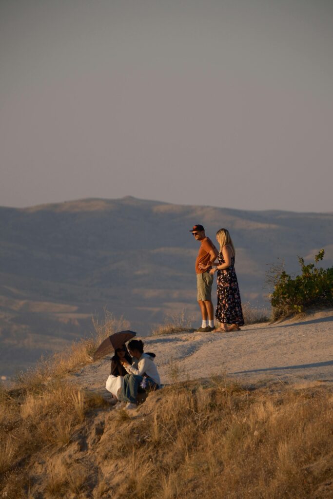 Tourists on a scenic hilltop enjoying a picturesque sunset view over rolling hills.