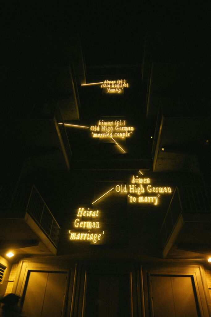 Stunning nighttime display of illuminated neon signs exploring German etymology on a building.