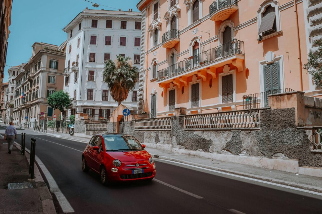 Red 5-door Hatchback On A Narrow Street Lined With Apartment Buildings