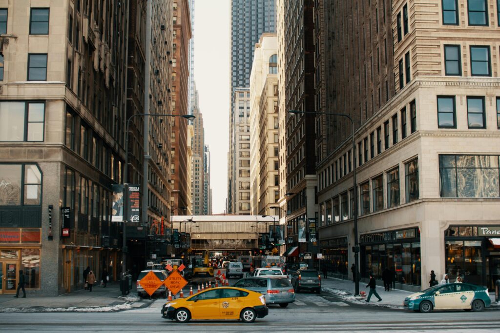 Cars driving on asphalt road between contemporary skyscrapers and buildings in New York City in daytime