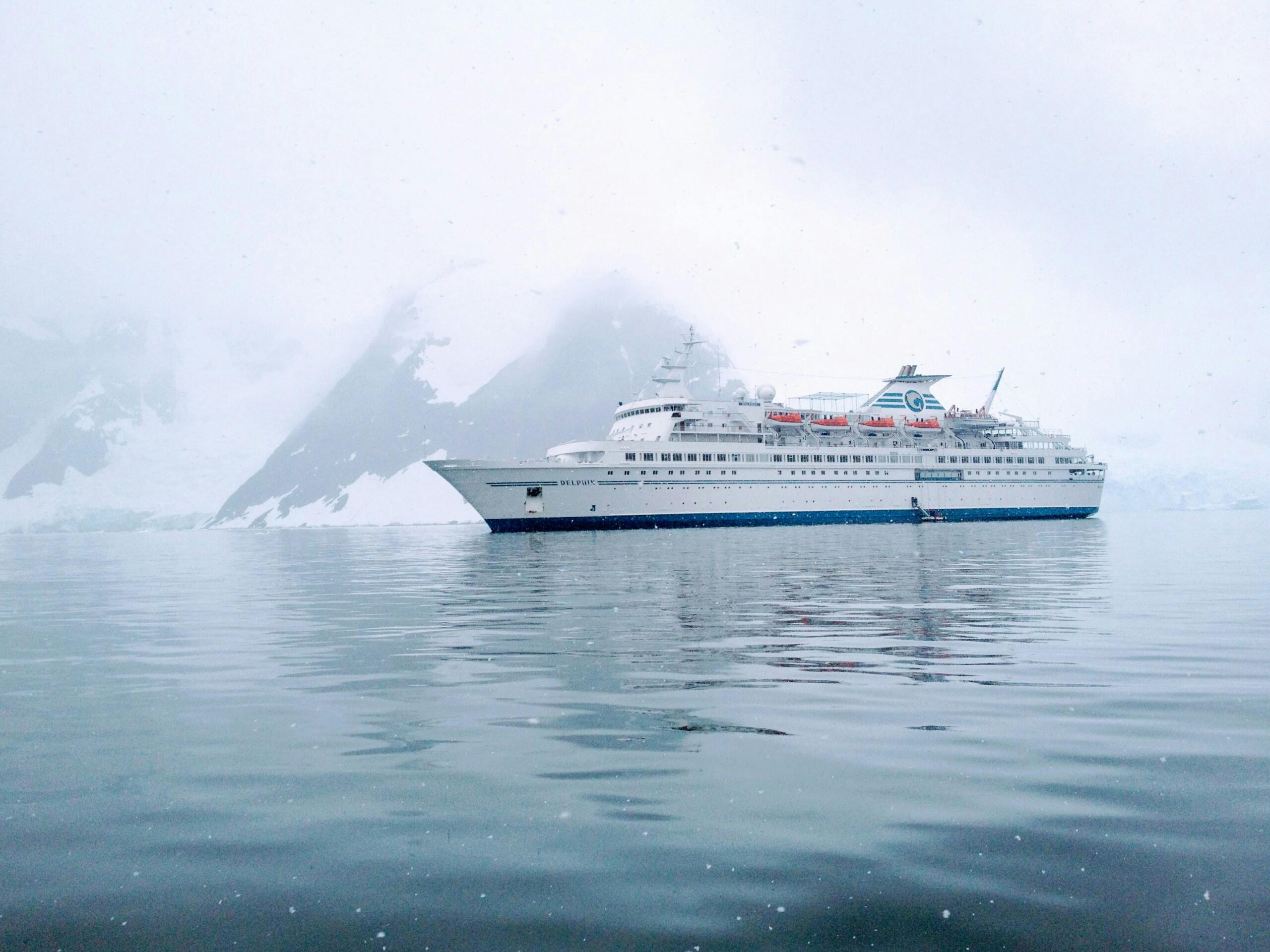 A cruise ship sails calmly through the icy waters of Antarctica, surrounded by snow-capped mountains.