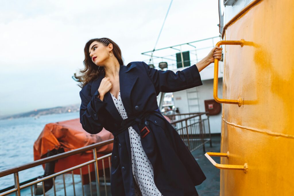 A fashionable woman in a coat poses on a ship deck, showcasing elegance and style.