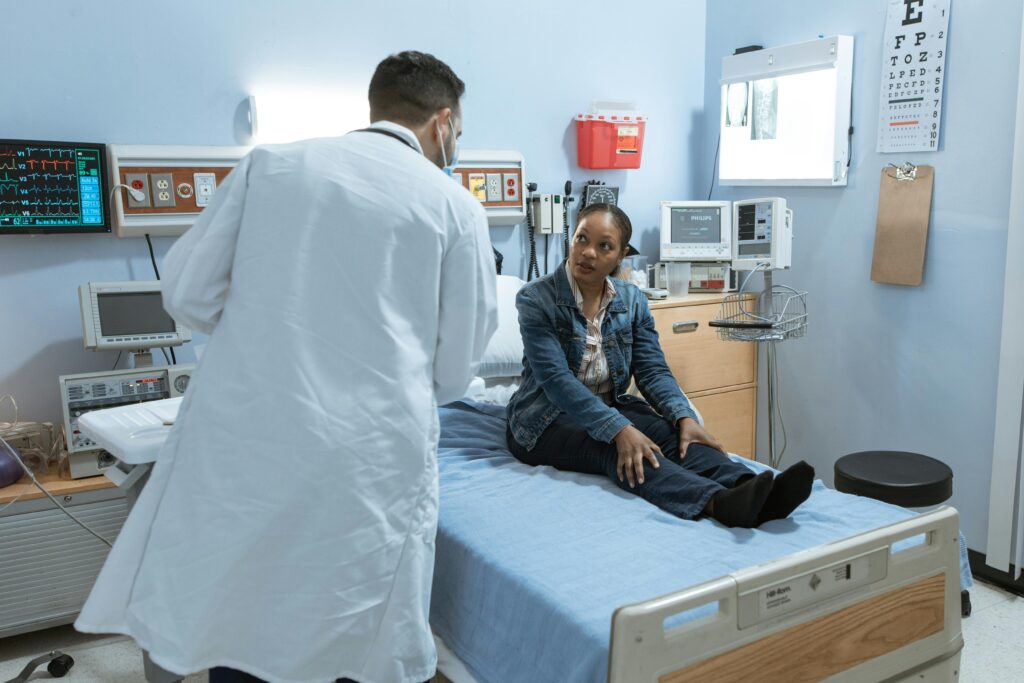 A doctor consults with a patient in a medical facility room, surrounded by healthcare equipment.