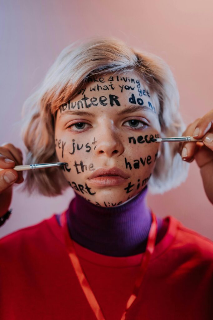 A young person with handwritten messages on their face in a creative, artistic portrait indoors.