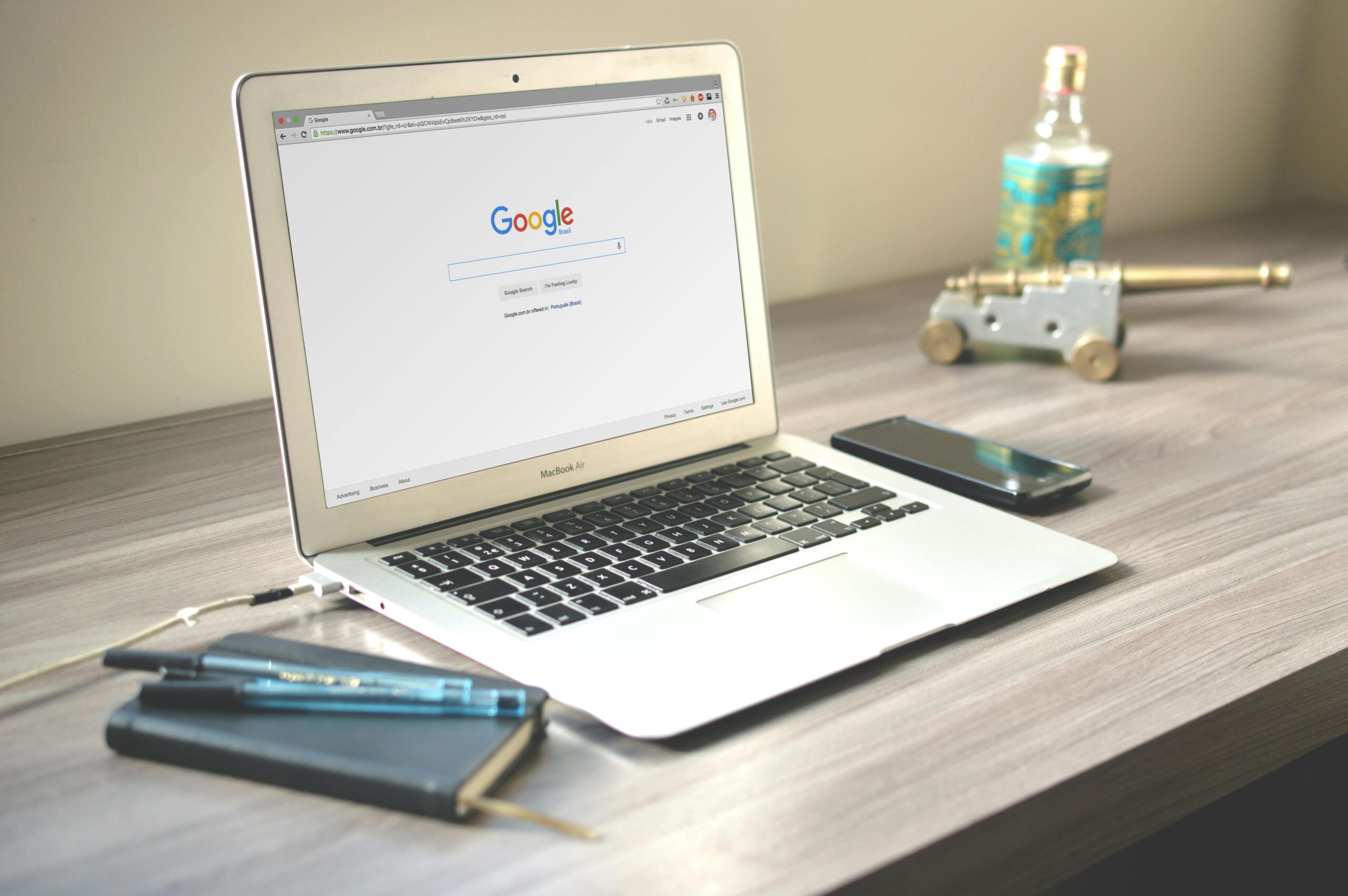 A neat workspace featuring a laptop displaying Google search, a smartphone, and a notebook on a wooden desk.