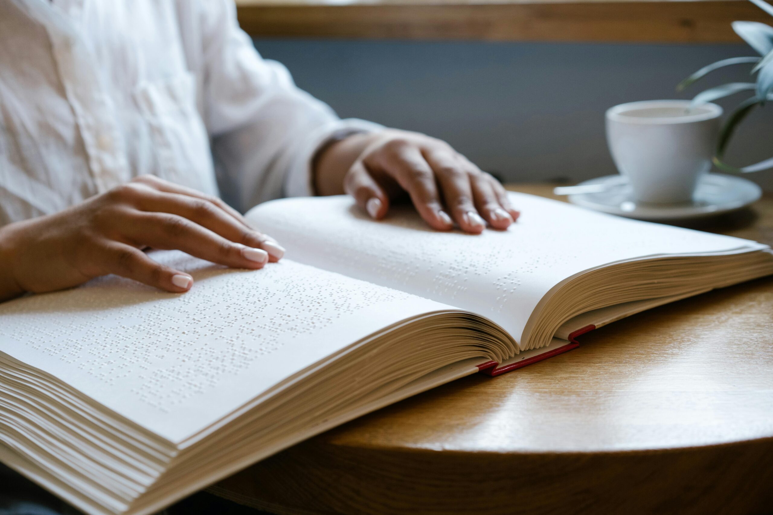 Close-up of hands reading a Braille book, emphasizing tactile learning and accessibility.