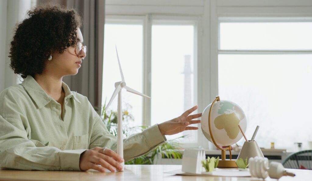 A young woman explores renewable energy with a globe and wind turbine model indoors.