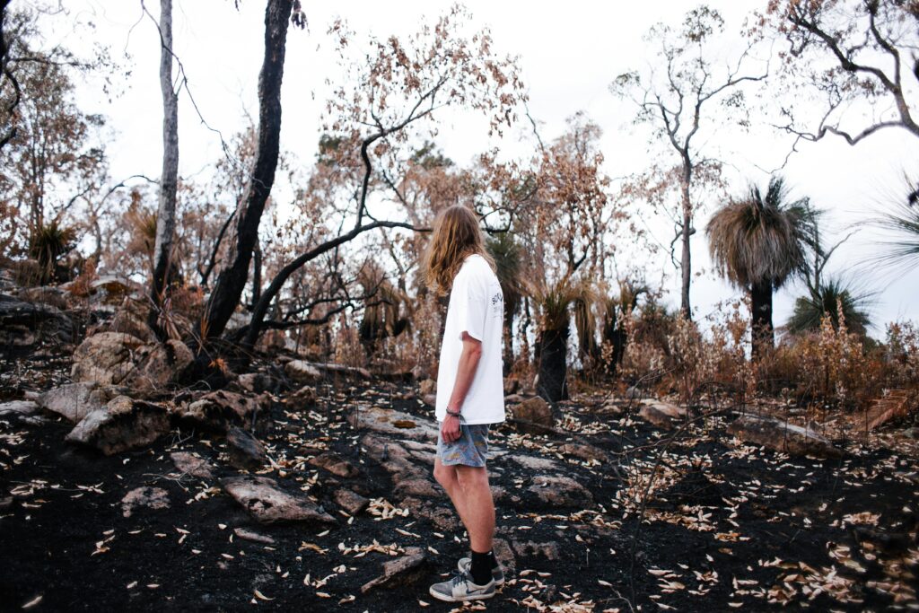 A man with long hair walks through a burned forest area, showcasing natural recovery.