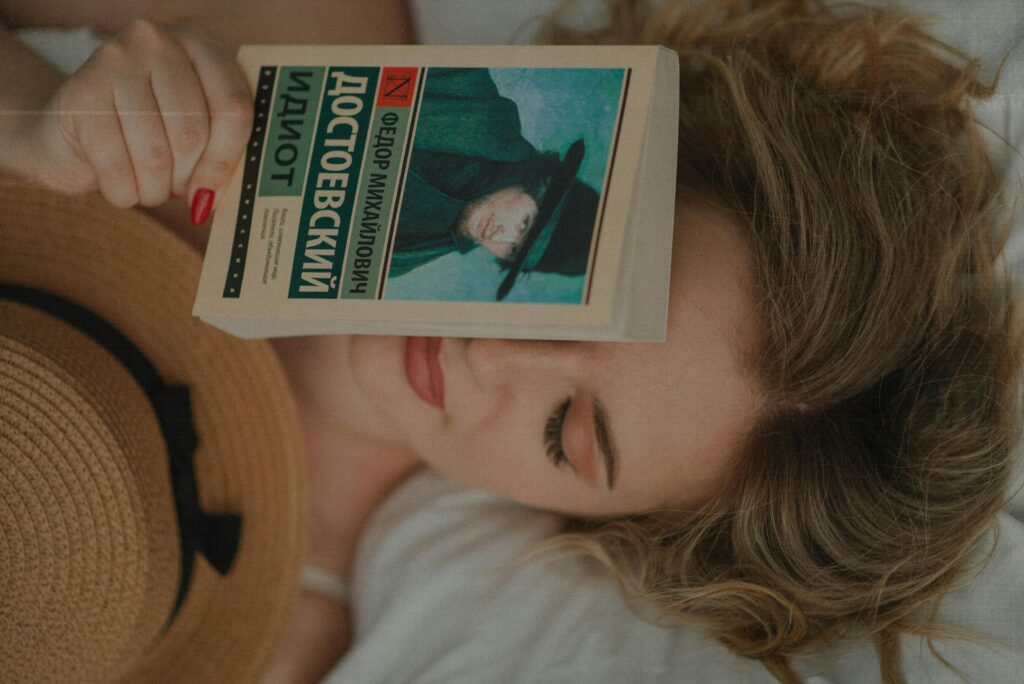 A woman lying down indoors with a Dostoevsky book covering part of her face, exuding relaxation and contemplation.