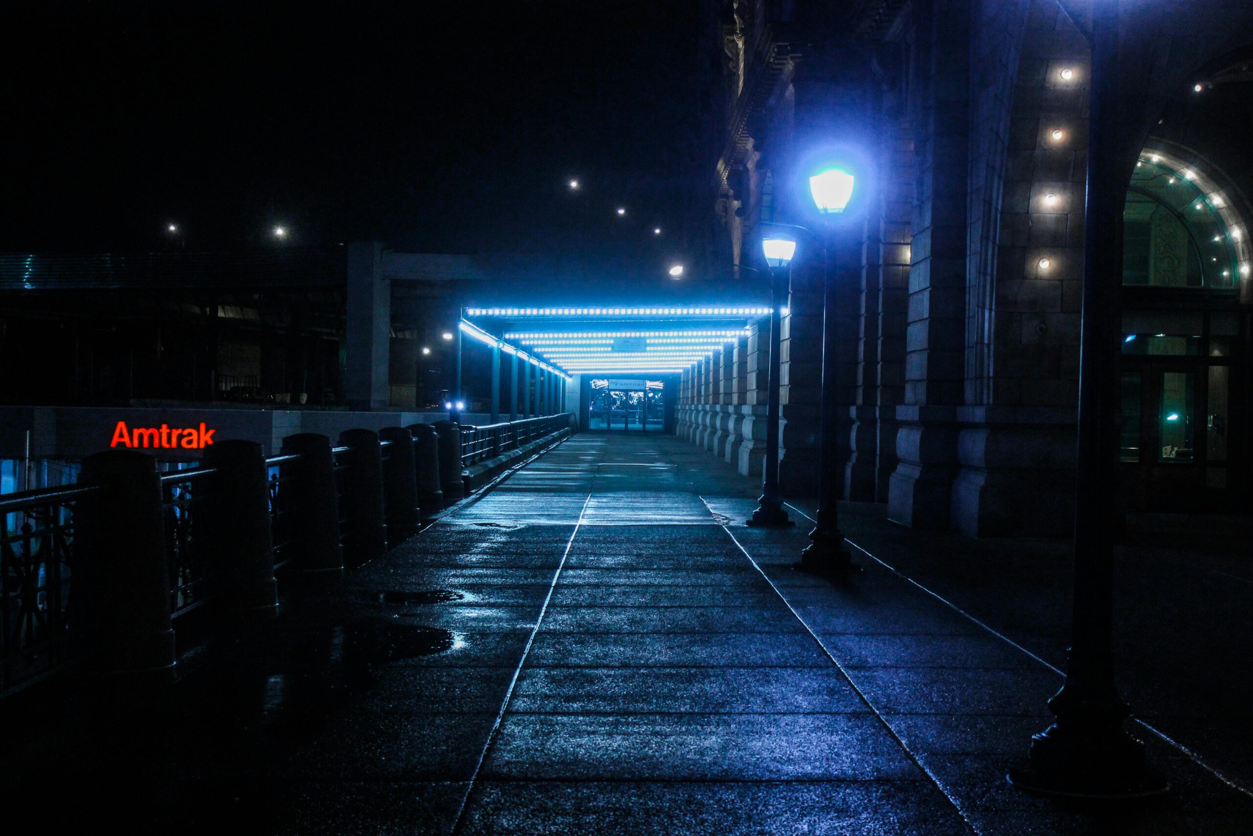 A moody, illuminated pathway at a train station during night with glowing lamps.