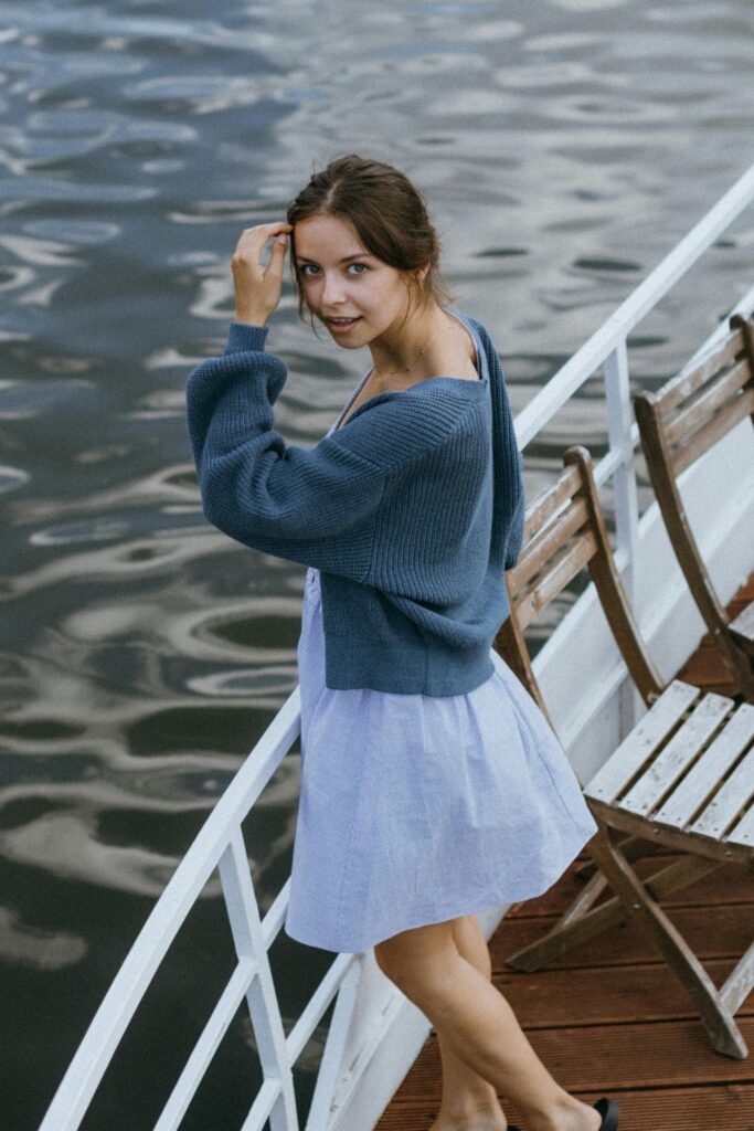 Young woman in blue cardigan enjoys a peaceful boat ride on a river, looking over her shoulder.