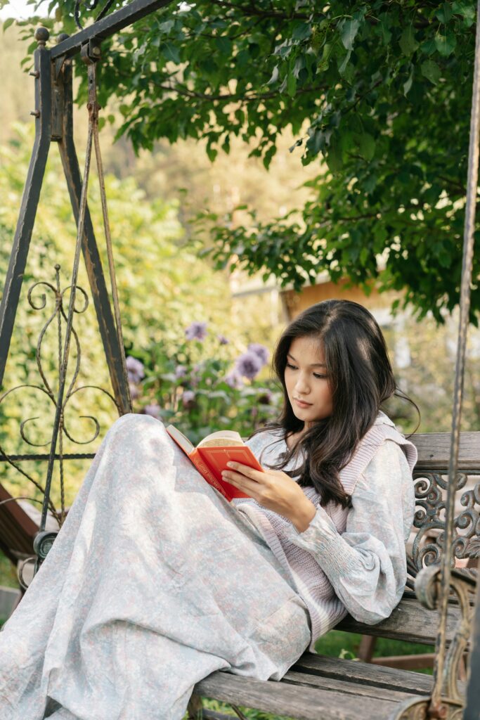 A serene portrait of a young woman reading a book on a garden swing surrounded by lush greenery.