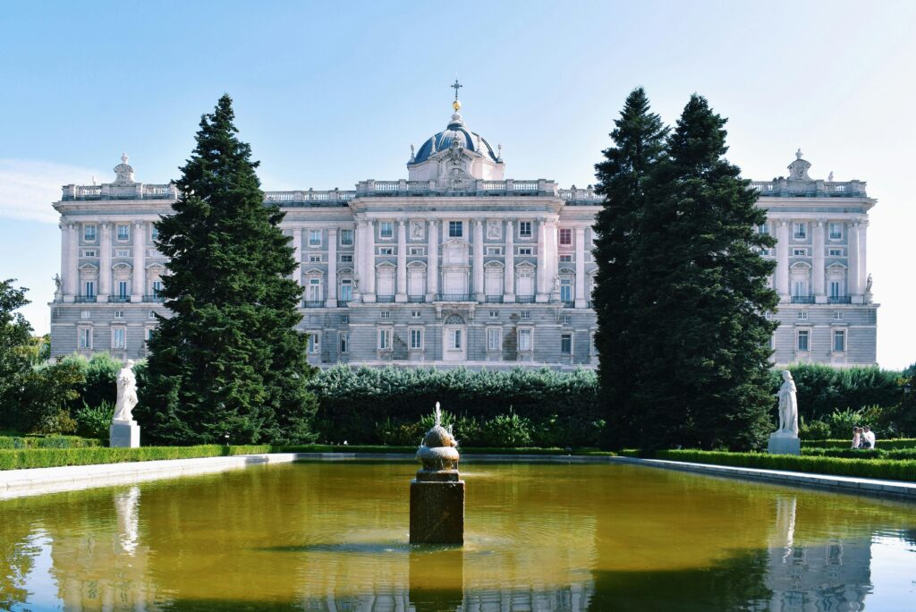 Stunning view of the Royal Palace in Madrid with a vibrant garden and pond in the foreground.