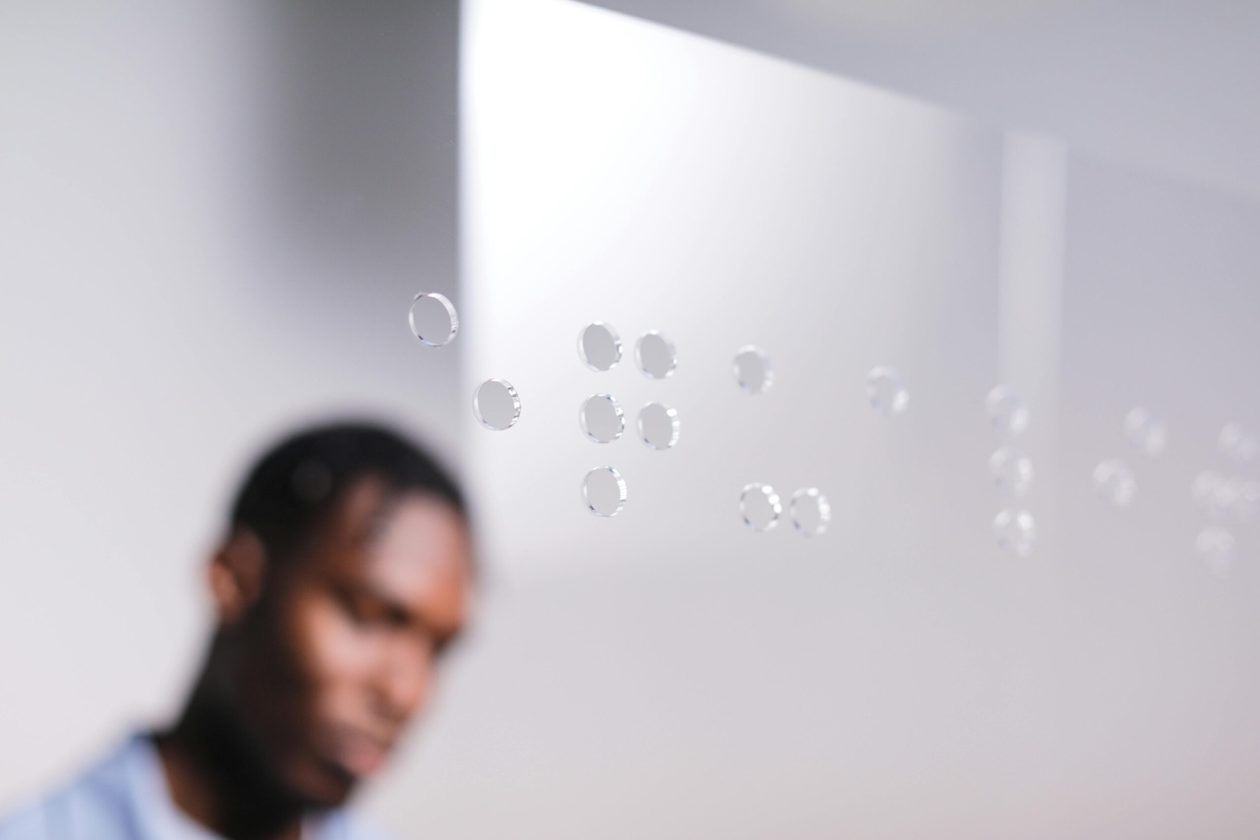 A man looking at a glass panel with Braille dots in a well-lit indoor space.