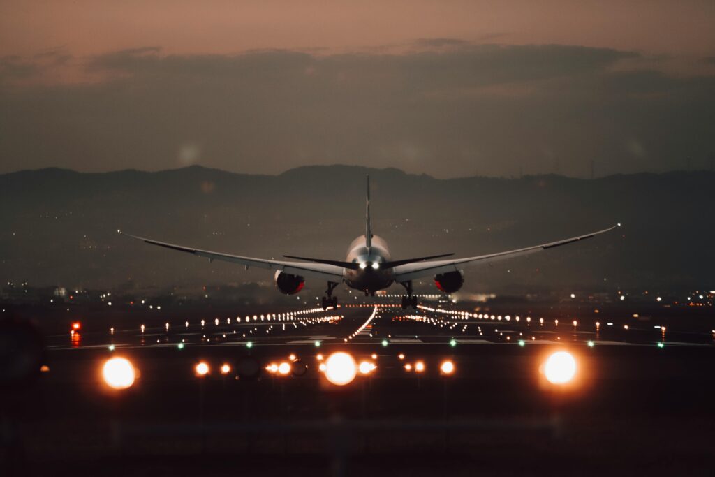 A large airplane makes a dramatic landing on a lit runway at twilight with a scenic mountain backdrop.