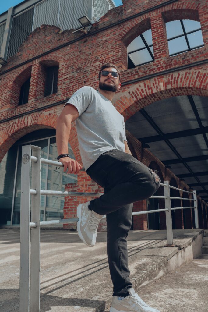 Confident man in sunglasses posing by a modern brick building, showcasing urban fashion.