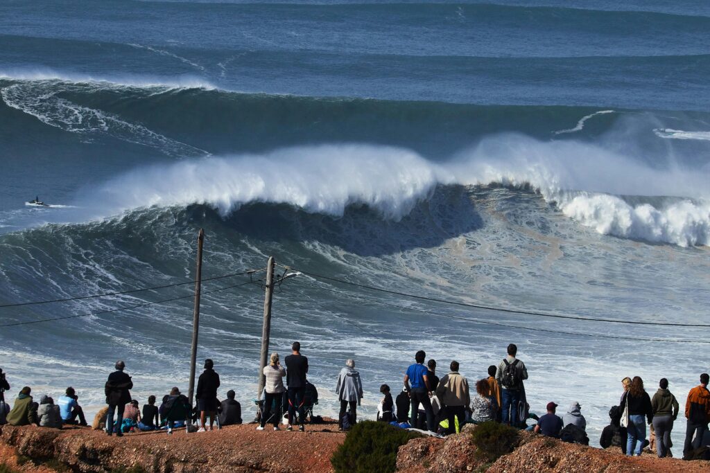 Thrilling view of spectators observing huge waves at Nazaré, a famous surfing location in Portugal.