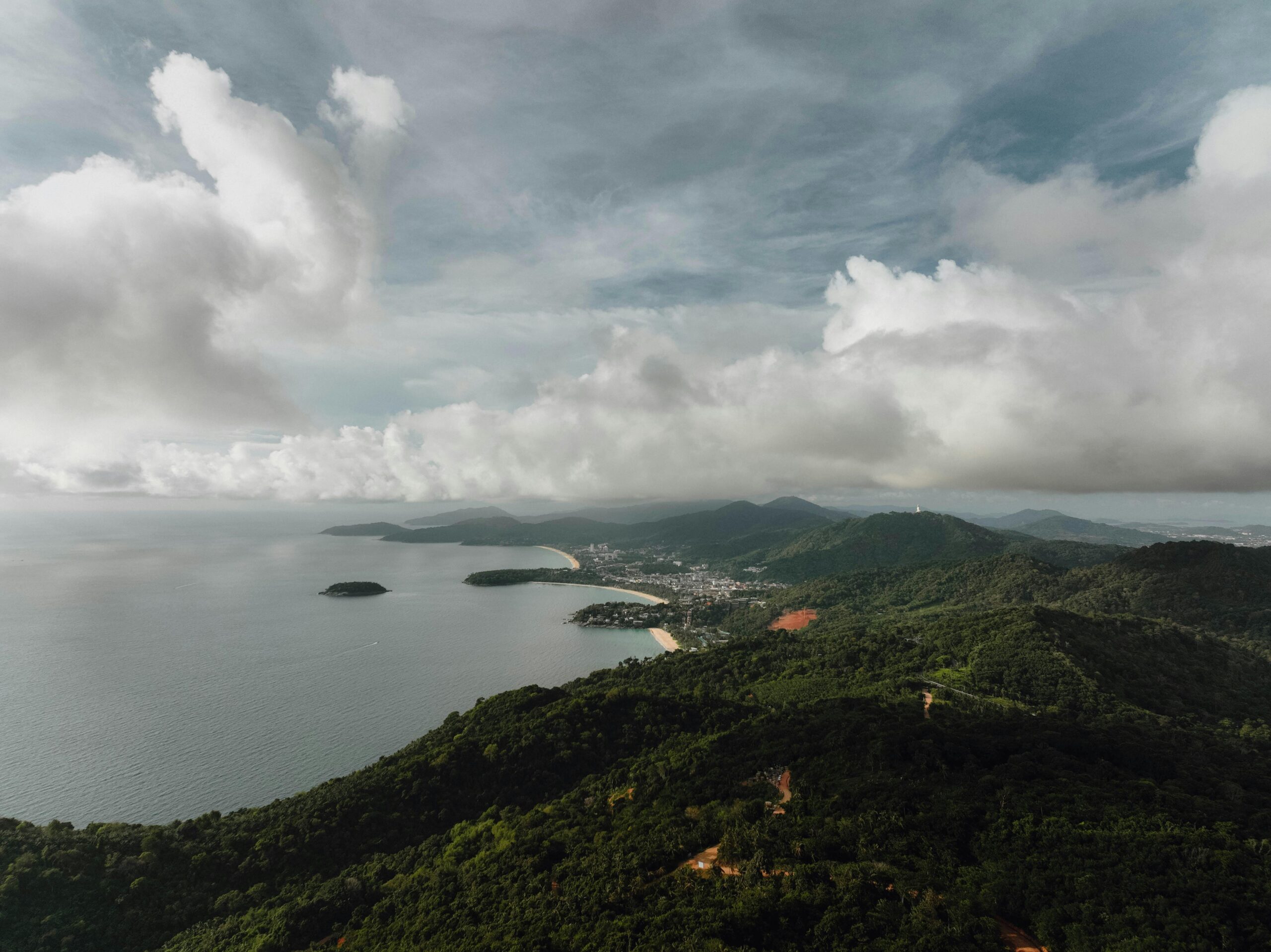 Stunning aerial view of Phuket's lush hills and coastline under a cloudy sky.