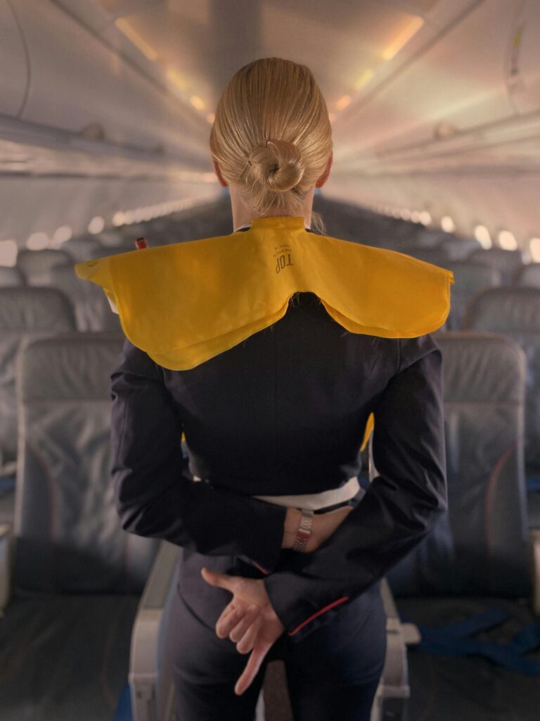 Back view of a stewardess standing in an airplane, demonstrating safety instructions with a life jacket.