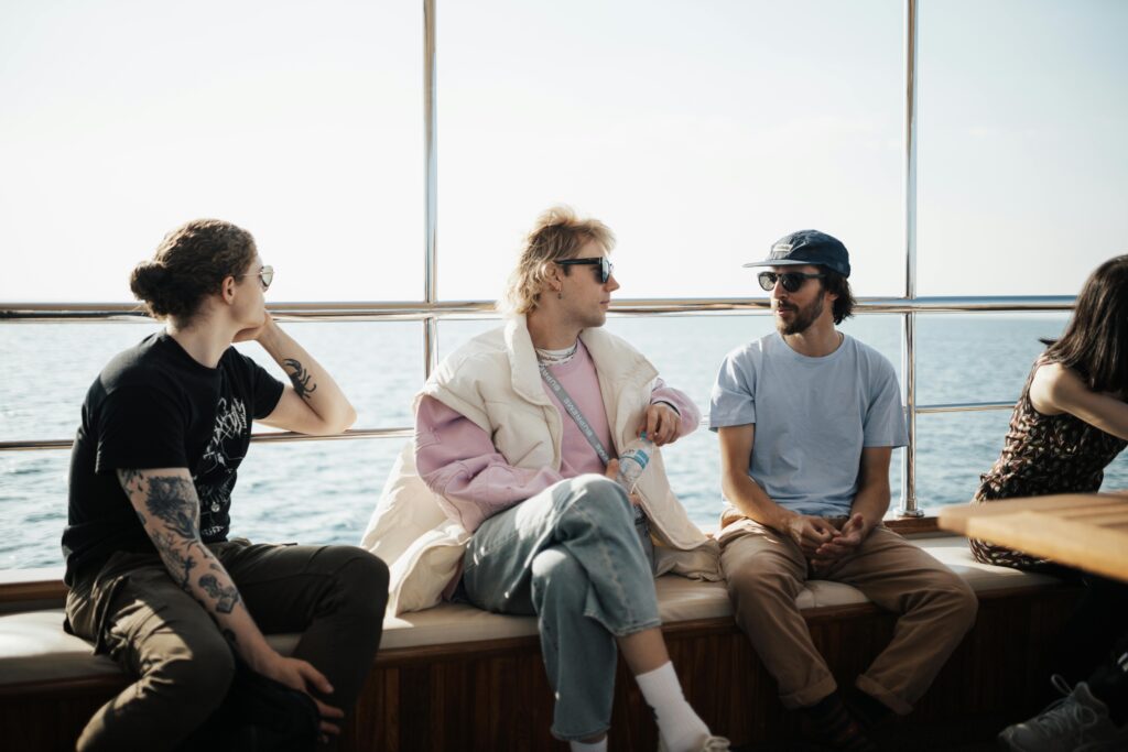 A group of young adults enjoying a relaxed conversation on a yacht deck with an ocean view.