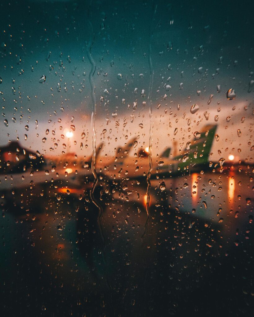 Blurry view of airplanes at the airport through a rain-soaked window at dusk.