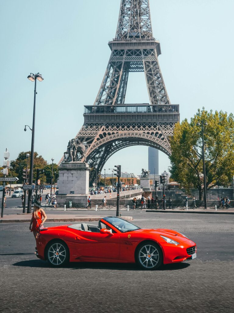 A vibrant red Ferrari parked in front of the iconic Eiffel Tower on a sunny day.