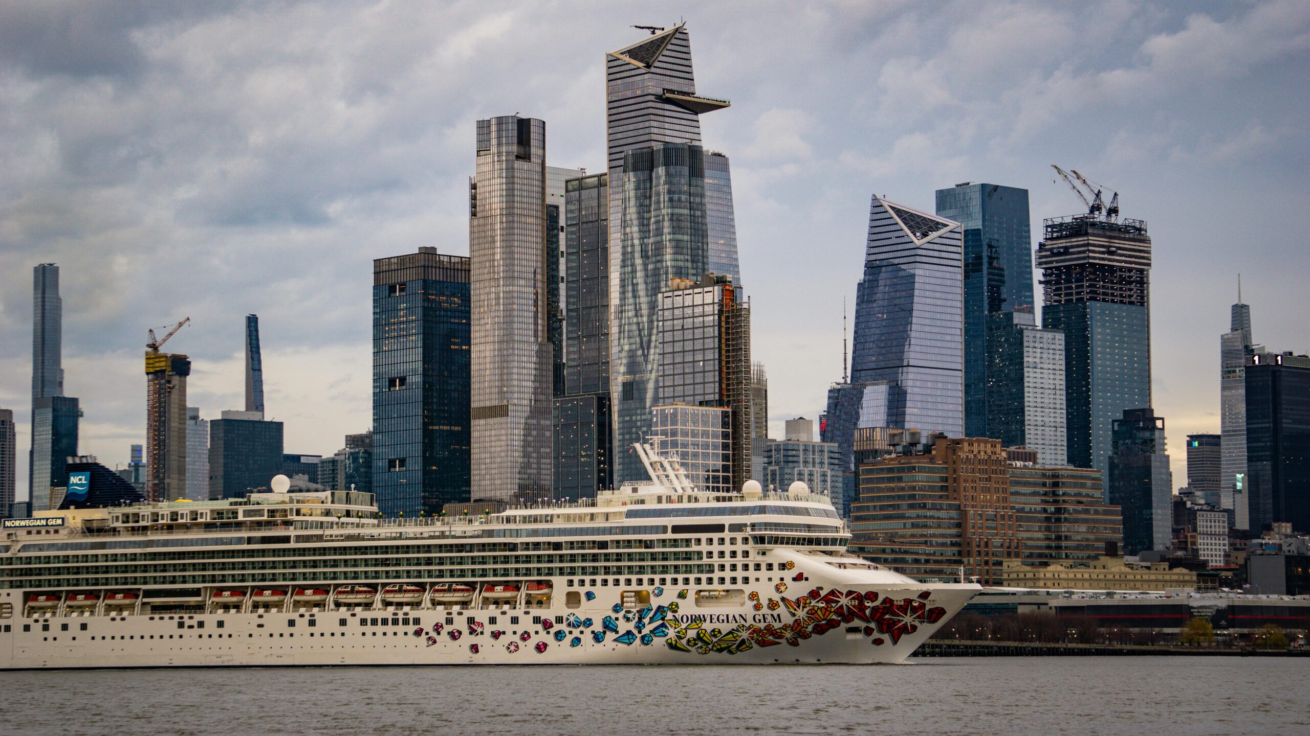 Norwegian Gem cruising past the iconic skyline of New York City with modern skyscrapers.