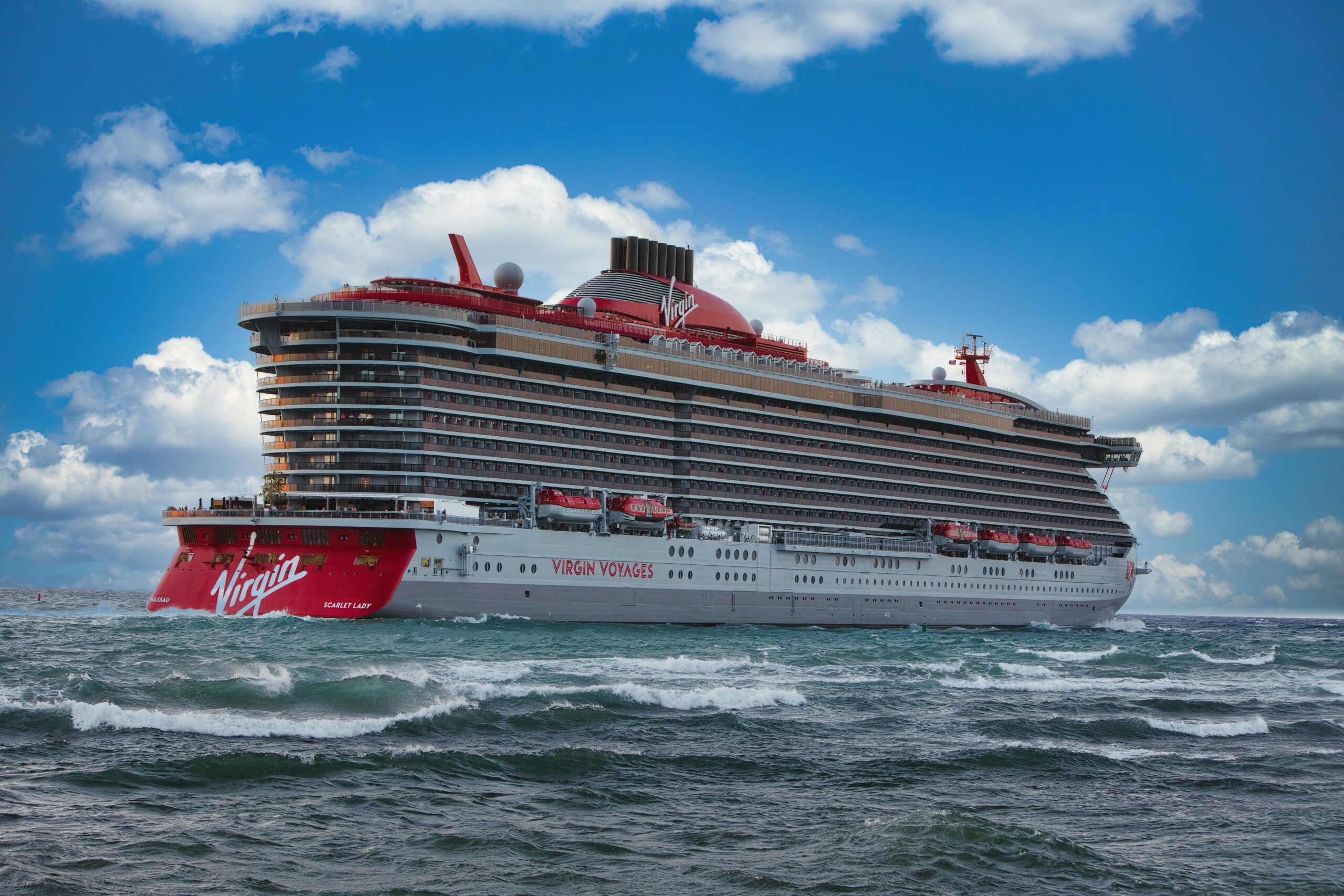 Experience the luxury of Virgin Voyages' Scarlet Lady cruise ship sailing through vibrant ocean waters.